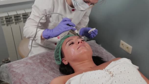 Cosmétologue professionnelle femme faisant nettoyage du visage par ultrasons au patient. — Video