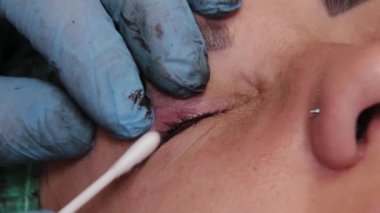 Güzellik uzmanı, güzellik salonundaki kadın müşterinin göz kapaklarındaki boyaları temizlemek için küçük pamuk çubukları kullanıyor..