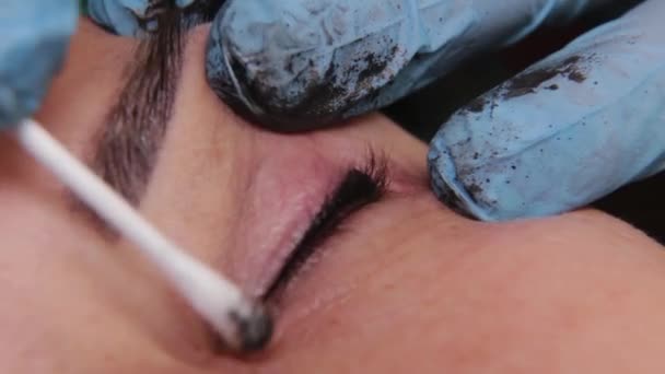 Esteticista está usando pequeno cotonete para remover o corante das pálpebras do cliente feminino em um salão de beleza . — Vídeo de Stock