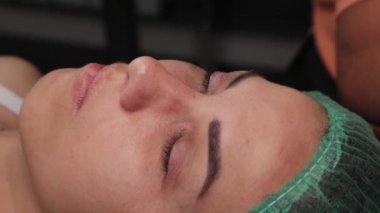 Güzellik uzmanı, güzellik salonundaki kadın müşterinin göz kapaklarındaki boyaları temizlemek için küçük pamuk çubukları kullanıyor..