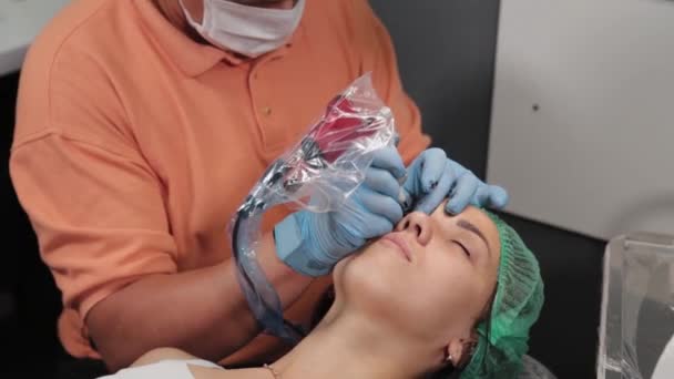 Un maquillador permanente se hace un tatuaje en los párpados superiores de una mujer. — Vídeos de Stock