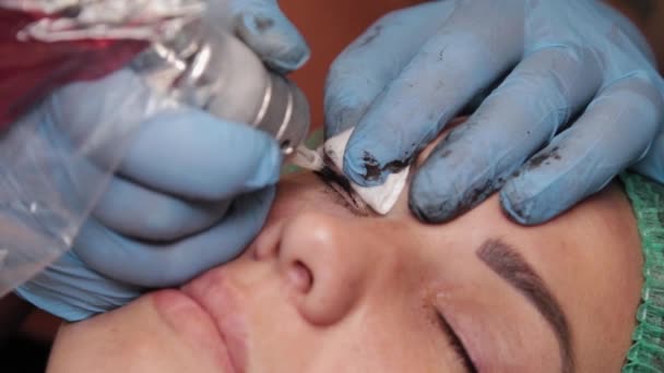Um artista de maquiagem permanente faz uma tatuagem em pálpebras superiores femininas. — Vídeo de Stock