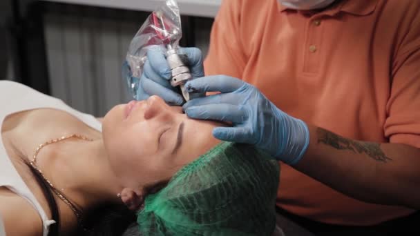 Een permanente make-up kunstenaar krijgt een tatoeage op een vrouw bovenste oogleden. — Stockvideo