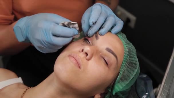 Un maquillador permanente se hace un tatuaje en los párpados superiores de una mujer. — Vídeos de Stock