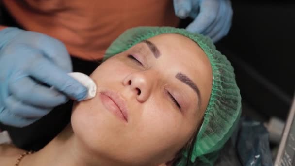 Beautician is using small cotton swab for remove dye from eyelids of female client in a beauty salon. — Stock Video