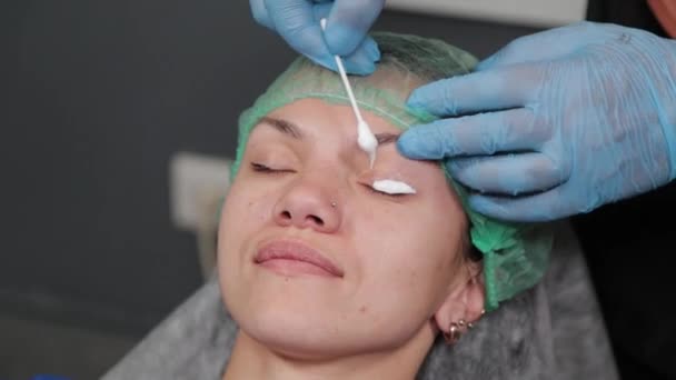O artista de maquiagem permanente aplica um anestésico às pestanas. — Vídeo de Stock