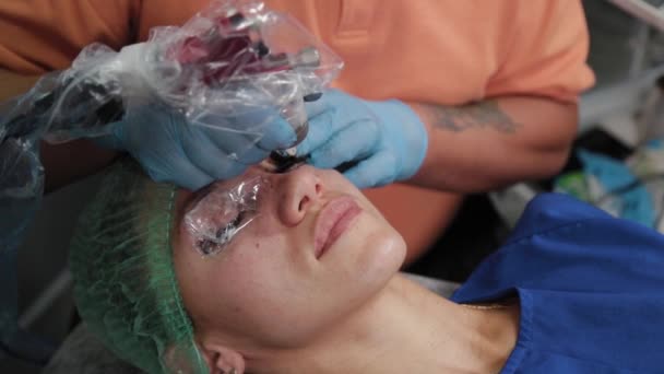 Um artista de maquiagem permanente faz uma tatuagem em pálpebras superiores femininas. — Vídeo de Stock