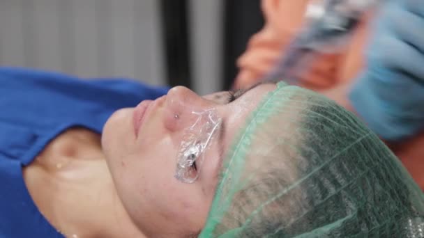 Een permanente make-up kunstenaar krijgt een tatoeage op een vrouw bovenste oogleden. — Stockvideo