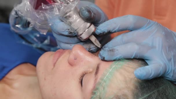 Un maquillador permanente se hace un tatuaje en los párpados superiores de una mujer. — Vídeo de stock