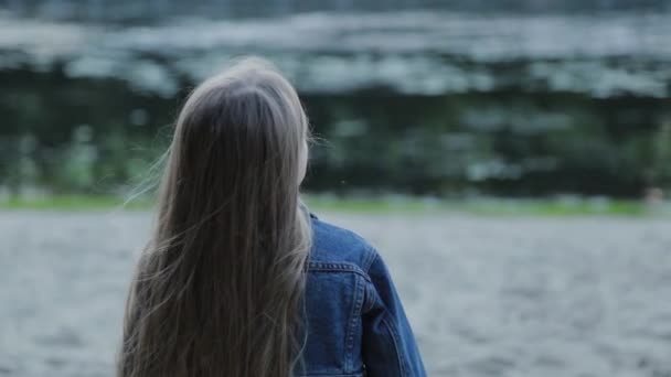 Красива дівчина сидить на лавці біля річки на пляжі . — стокове відео