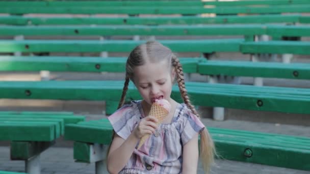 Hermosa chica feliz comiendo helado en el parque en un banco. — Vídeo de stock