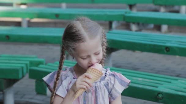 Piękna szczęśliwa dziewczyna jedząca lody w parku na ławce. — Wideo stockowe