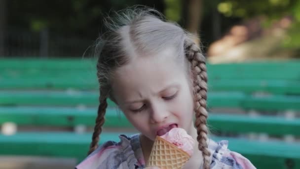 Krásná šťastná dívka jíst zmrzlinu v parku na lavičce.