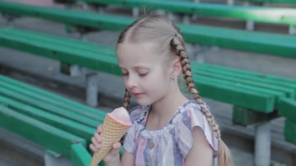 Menina feliz bonita comer sorvete no parque em um banco. — Vídeo de Stock