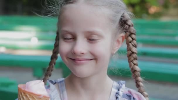Menina feliz bonita comer sorvete no parque em um banco. — Vídeo de Stock