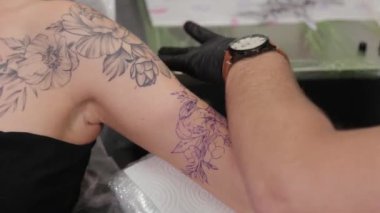 Dövme sanatçısı genç bir kızın kolunda dövme yapıyor..