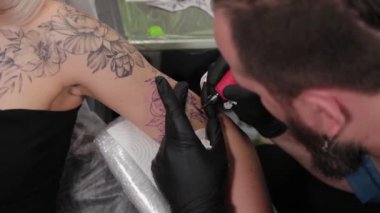 Dövme sanatçısı genç bir kızın kolunda dövme yapıyor..