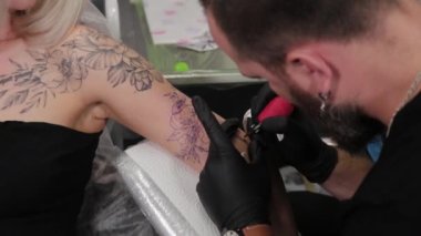 Dövme sanatçısı genç bir kızın kolunda dövme yapıyor..