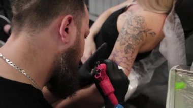 Dövme sanatçısı genç bir kızın kolunda dövme yapıyor..