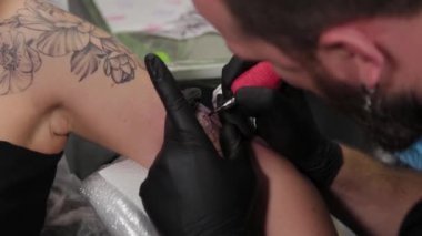 Dövme sanatçısı genç bir kızın kolunda dövme yapıyor..