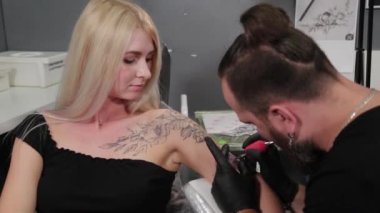 Dövme sanatçısı genç bir kızın kolunda dövme yapıyor..