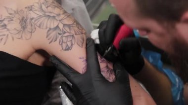 Dövme sanatçısı genç bir kızın kolunda dövme yapıyor..
