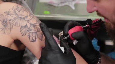 Dövme sanatçısı genç bir kızın kolunda dövme yapıyor..