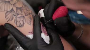 Dövme sanatçısı genç bir kızın kolunda dövme yapıyor..