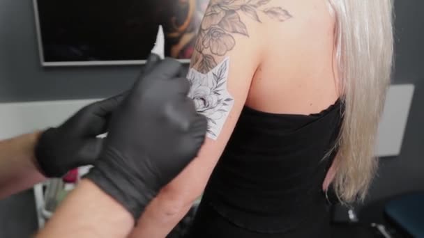 Le tatoueur colle un pochoir de tatouage à un bras de fille. — Video