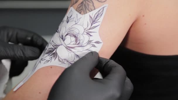 El tatuador pega una plantilla de tatuaje a un brazo de chicas. — Vídeos de Stock