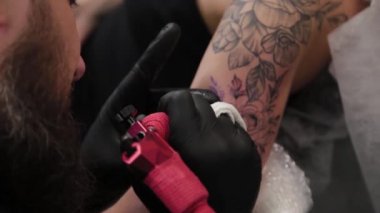 Dövme sanatçısı genç bir kızın kolunda dövme yapıyor..