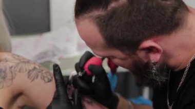 Dövme sanatçısı genç bir kızın kolunda dövme yapıyor..
