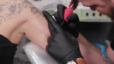 Dövme sanatçısı genç bir kızın kolunda dövme yapıyor..