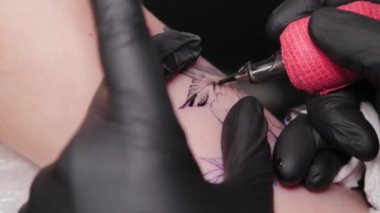 Dövme sanatçısı genç bir kızın kolunda dövme yapıyor..
