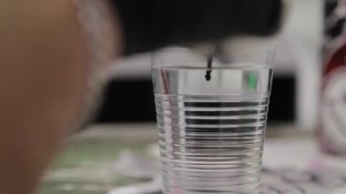 Dövme ustası mürekkebi dövme makinesinin suyuna karıştırıyor. Kırmızı arka planda pembe güvenlik eldivenleri. Kadın usta sanatçı..