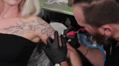 Dövme sanatçısı genç bir kızın kolunda dövme yapıyor..