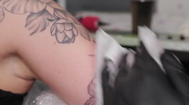 Dövme sanatçısı genç bir kızın kolunda dövme yapıyor..