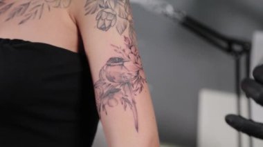 Dövme sanatçısı genç bir kızın kolunda dövme yapıyor..