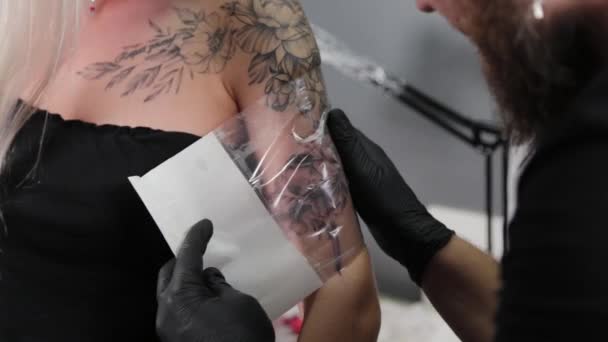De tatoeëerder bedekt de tatoeage met folie. — Stockvideo