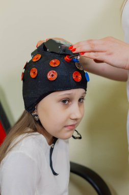 Bir kadın çocuk nörologu muayenehanede özel bir aletle bir kızı muayene ediyor..