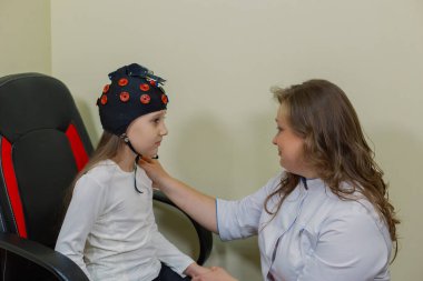 Bir kadın çocuk nörologu muayenehanede özel bir aletle bir kızı muayene ediyor..