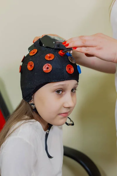 A woman childrens neurologist examines a girl in the office with a special device.