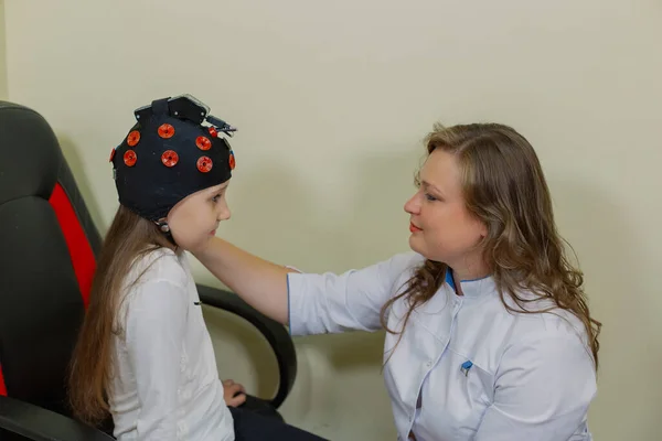 Uma mulher neurologista infantil examina uma menina no escritório com um dispositivo especial. — Fotografia de Stock