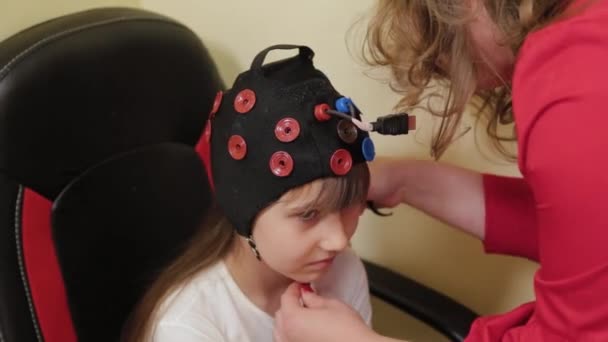 Préparation d'une analyse EEG du cerveau dans le bureau des médecins. Installation d'un dispositif d'examen électroencéphalographique d'une fille. — Video