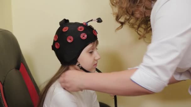 Preparando-se para uma análise EEG do cérebro no consultório médico. Instalação de um dispositivo para exame eletroencefalográfico de uma menina. — Vídeo de Stock