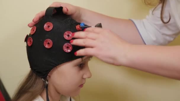 Preparando-se para uma análise EEG do cérebro no consultório médico. Instalação de um dispositivo para exame eletroencefalográfico de uma menina. — Vídeo de Stock