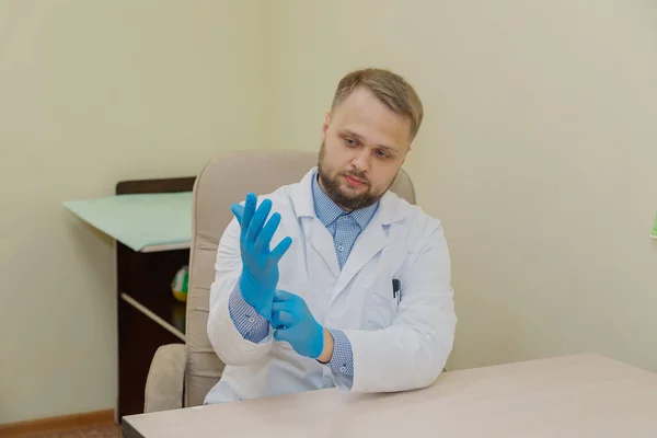 Мужчина-врач надевает резиновые перчатки в офисе. — стоковое фото
