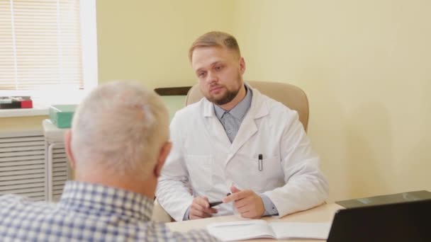 Männlicher Arzt im Gespräch mit einem älteren Patienten. — Stockvideo