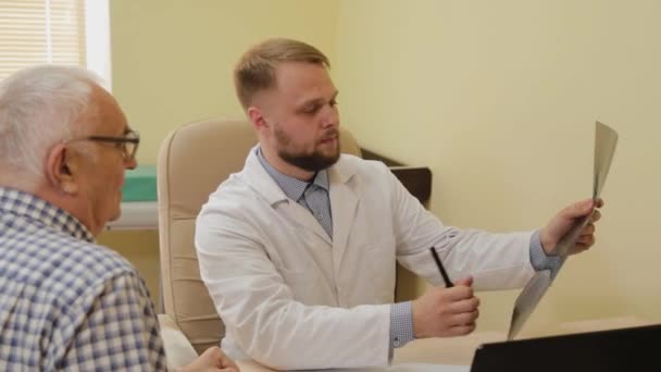 Männlicher Neurologe betrachtet ein Röntgenbild mit einem älteren Patienten. — Stockvideo