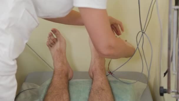 Vrouwelijke arts hecht contacten aan de benen van de patiënt. — Stockvideo